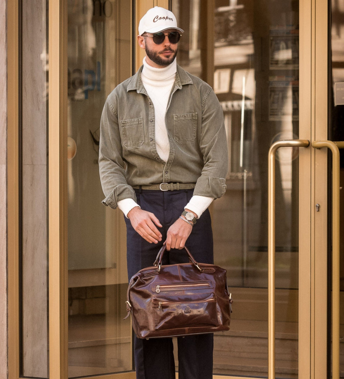 Man in an olive overshirt carrying the brown East of Eden leather bag by its handle