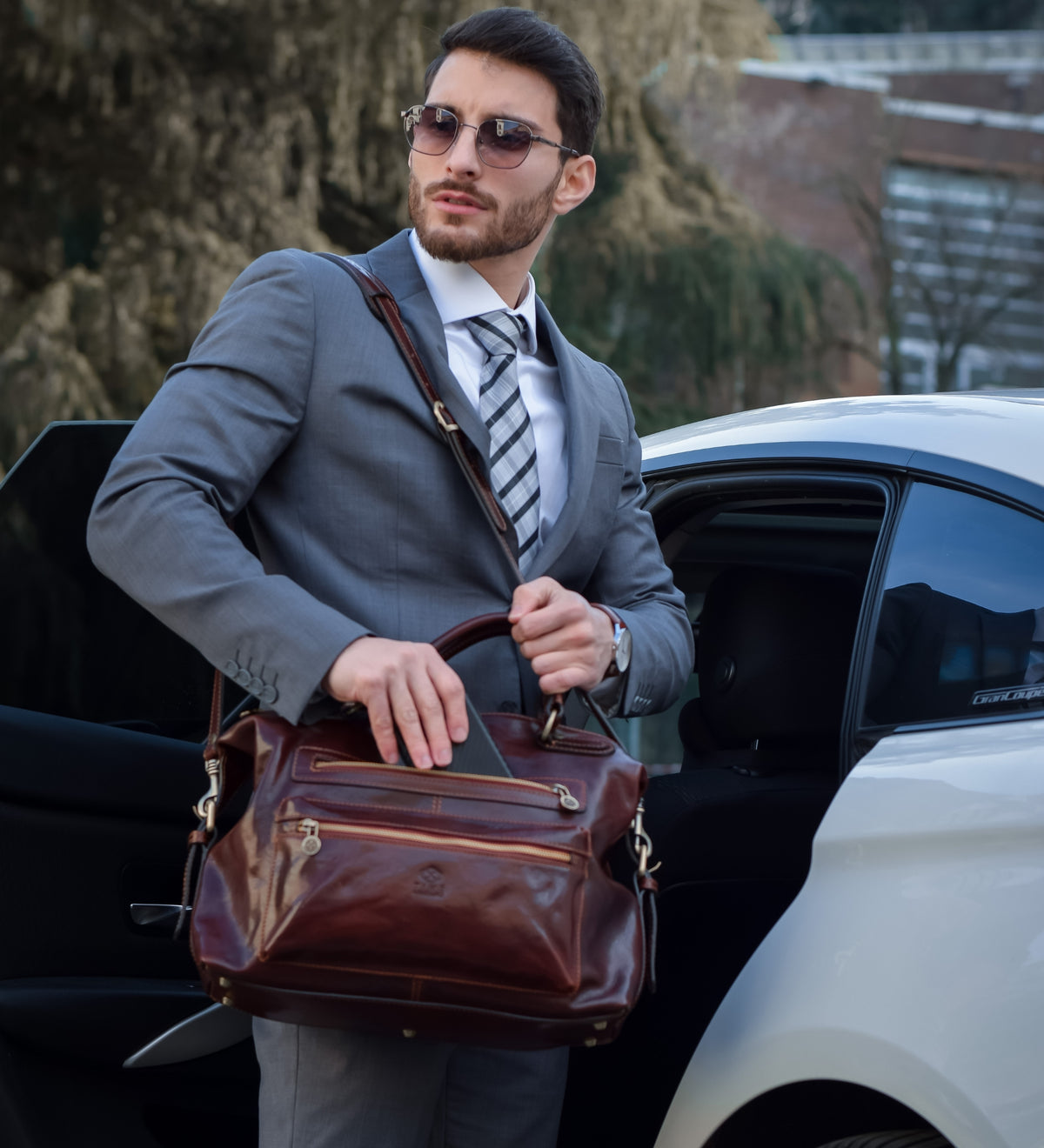 Man in a grey suit lifting the brown East of Eden leather bag from a car